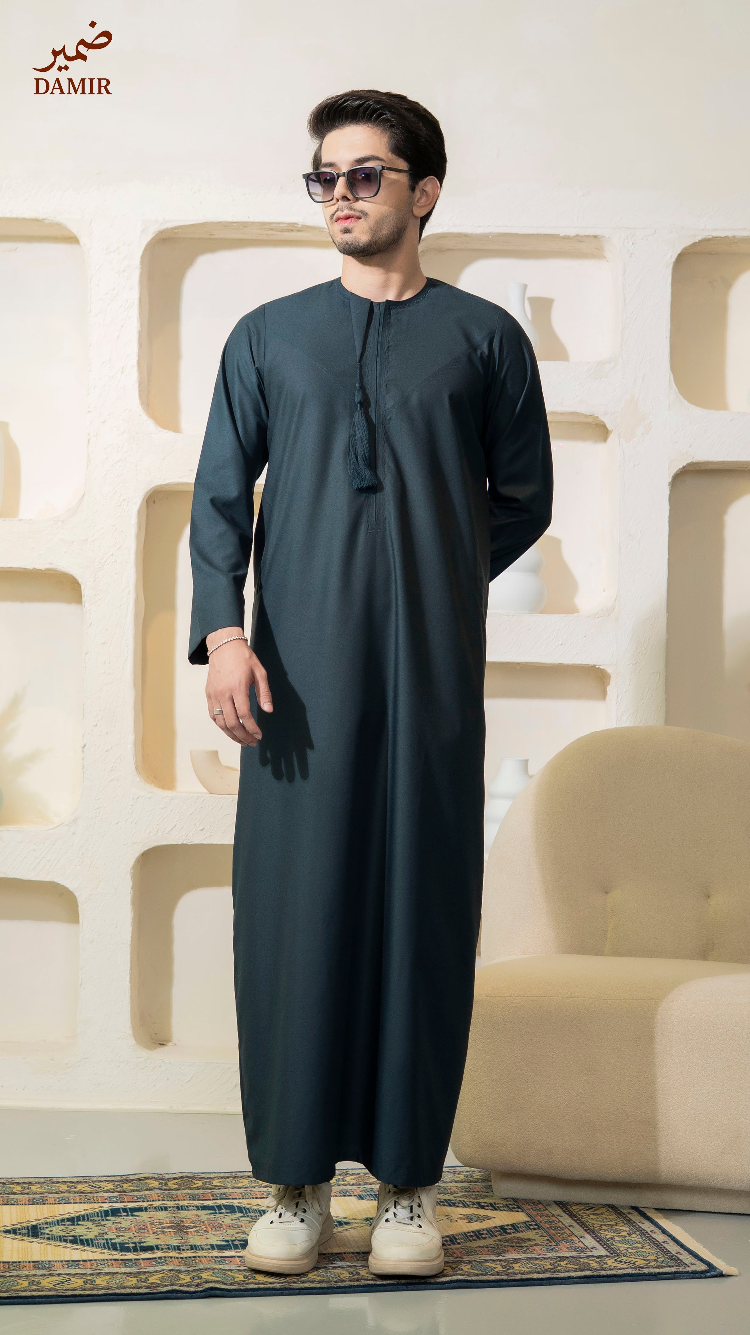 Man wearing a Teal traditional outfit with sunglasses in a room with decorative wall and furniture.