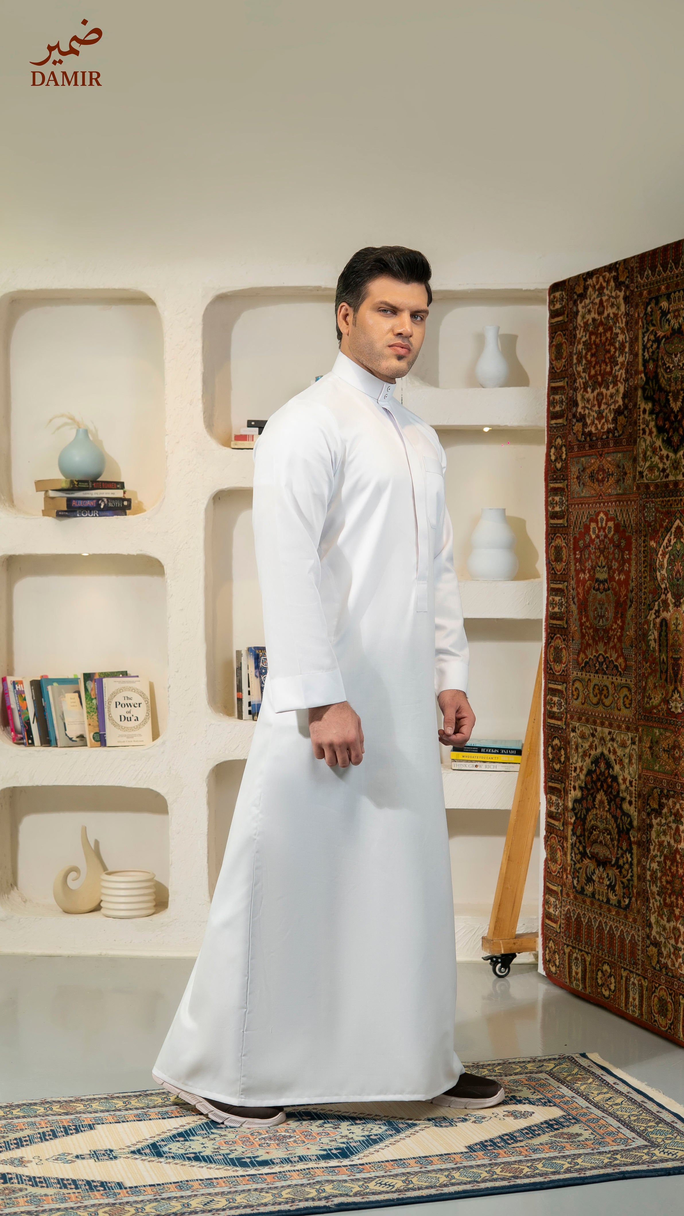Man wearing a white traditional outfit standing in a room with decorative elements.