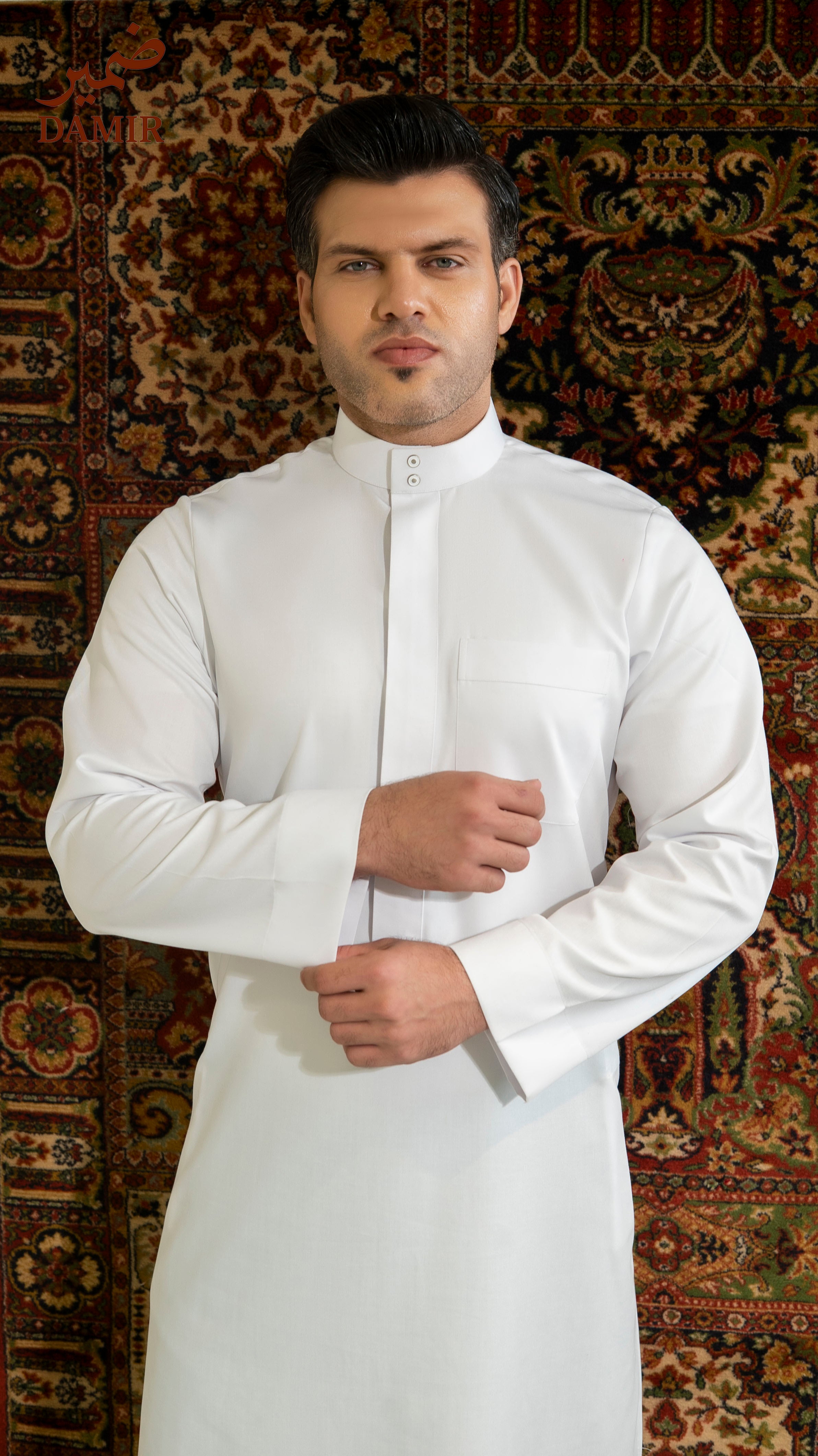 Man wearing a white traditional outfit against a patterned rug background