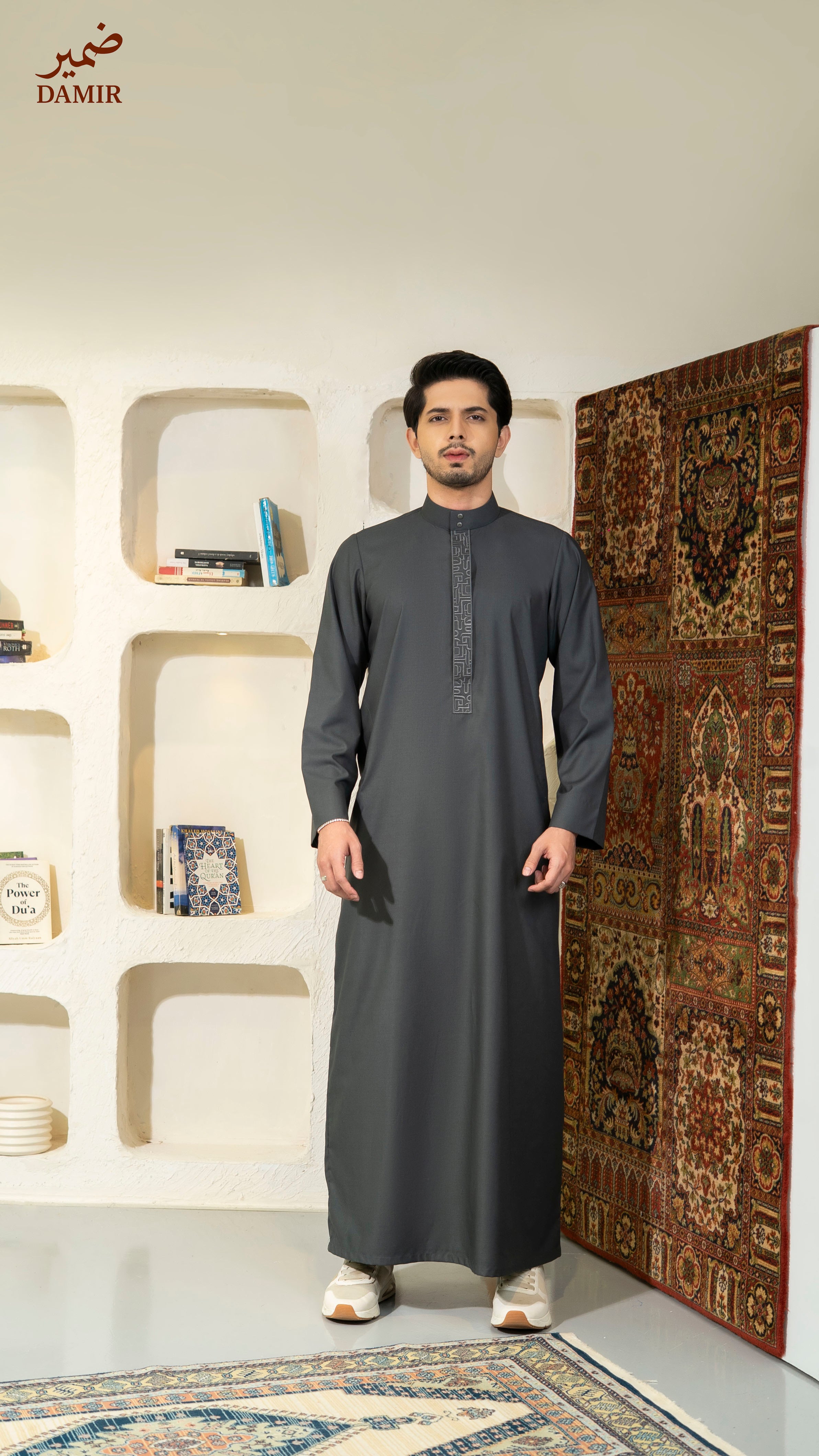 Man wearing a dark gray traditional outfit standing in a room with decorative elements.