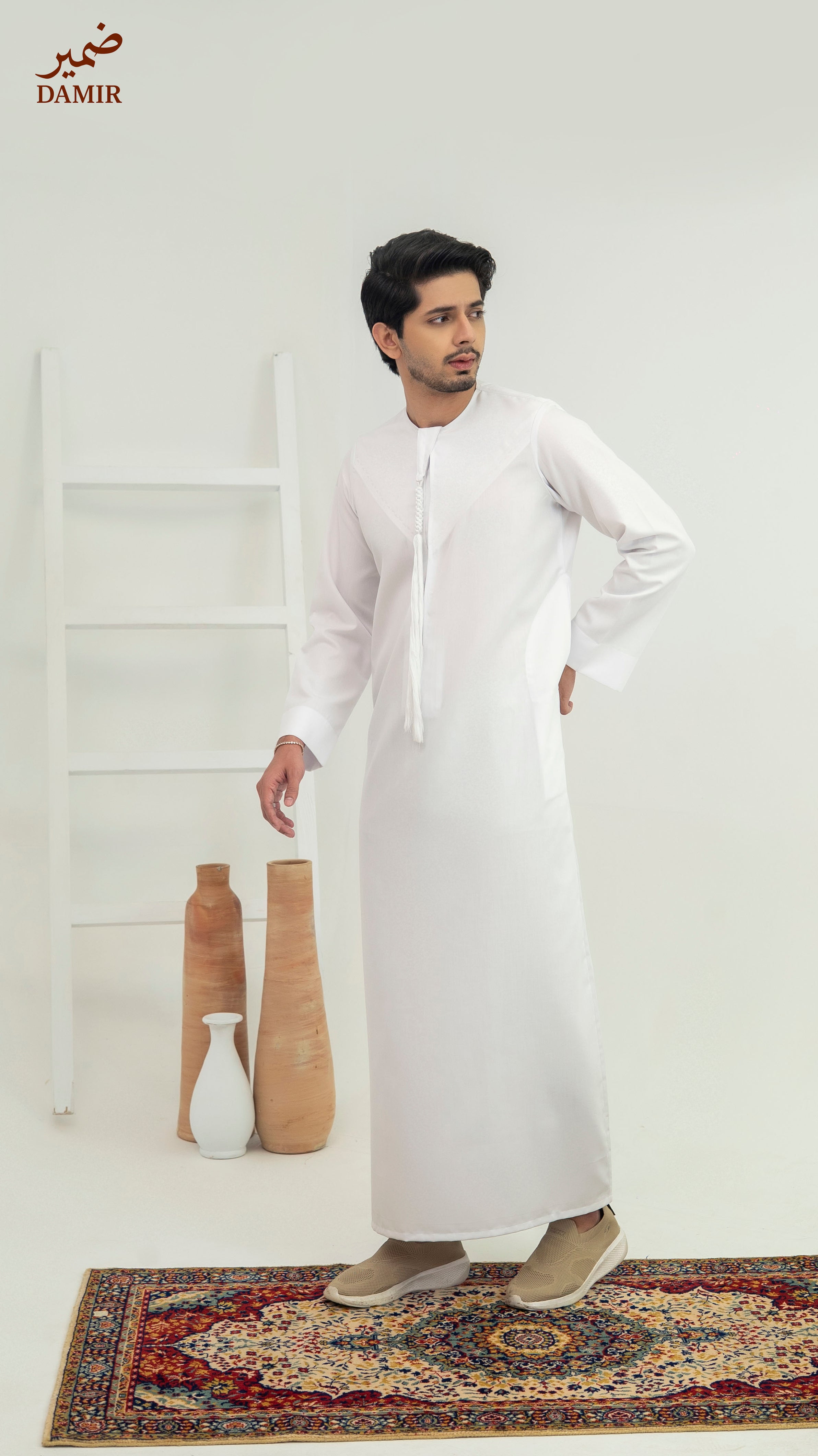 Man wearing a white traditional outfit standing in a minimalistic room with decorative vases.