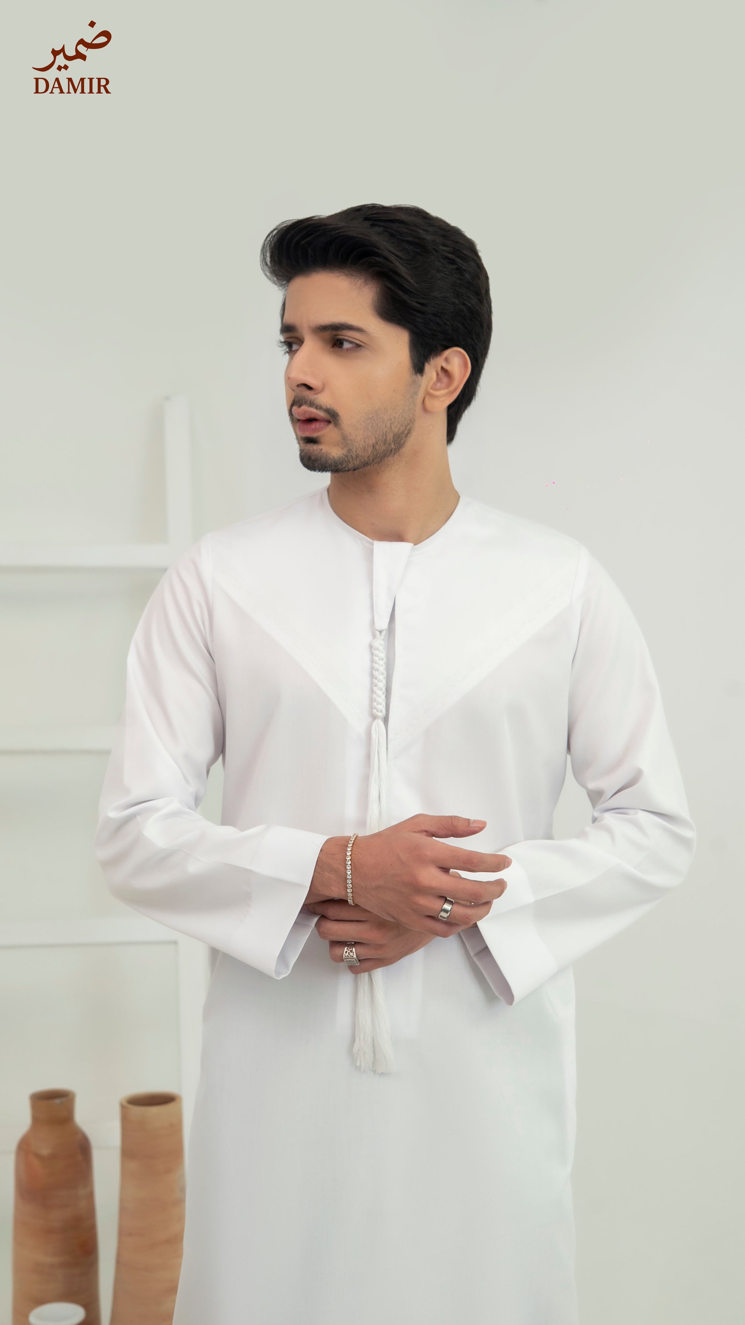 Man wearing a white traditional outfit with 'DAMIR' branding in the corner.