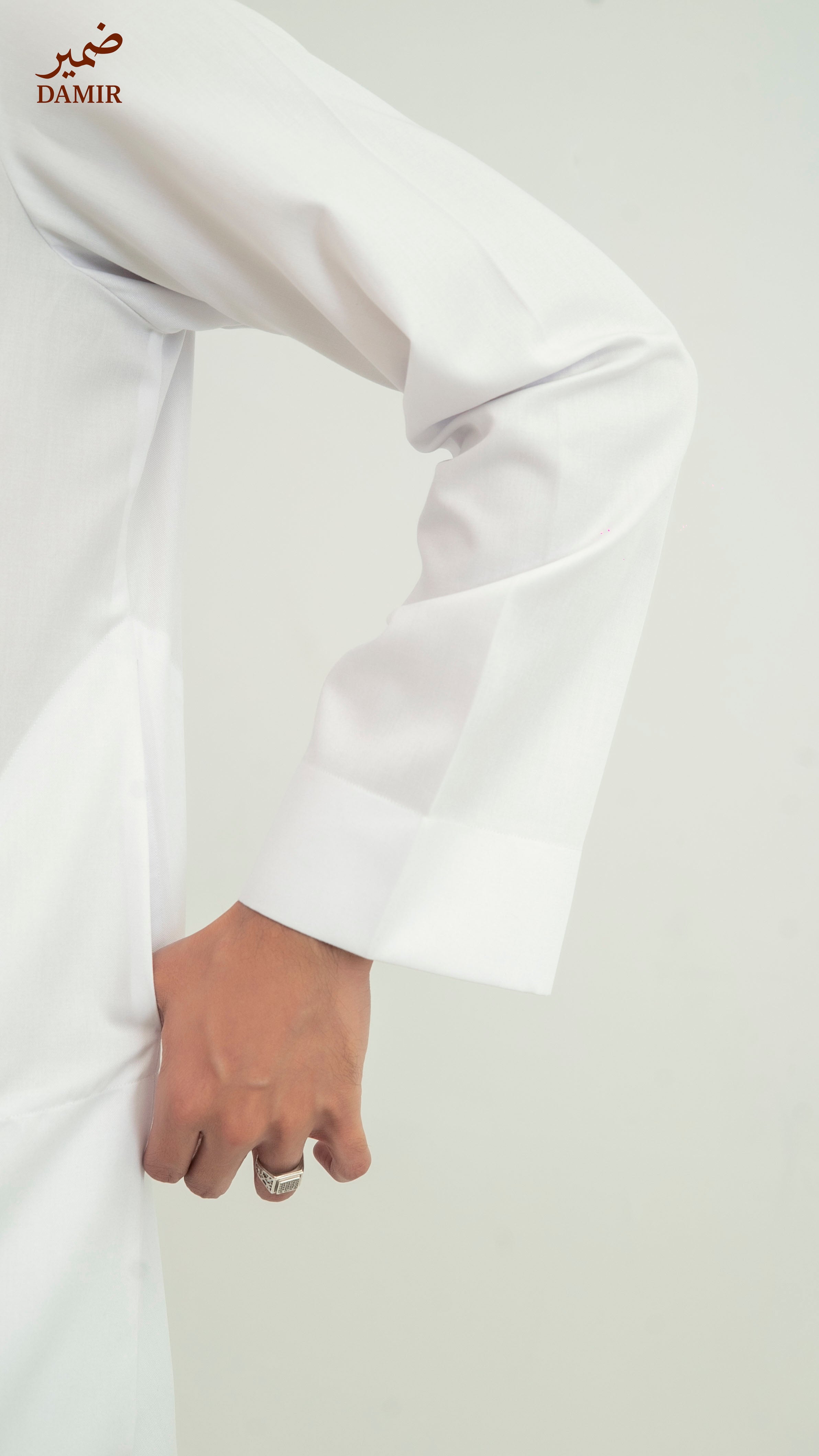 White garment with a hand holding it, on a plain background